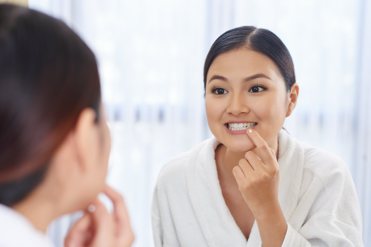 Woman looking in a mirror and examining a tooth she would like to improve.