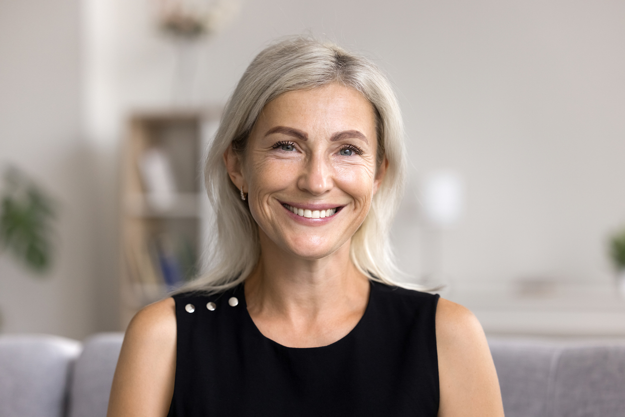 Woman with gray hair smiling confidently, with an even, bright smile.